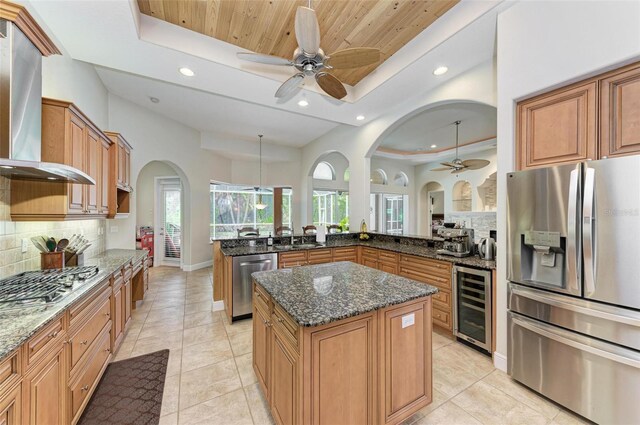 kitchen featuring extractor fan, a kitchen island, a tray ceiling, appliances with stainless steel finishes, and beverage cooler