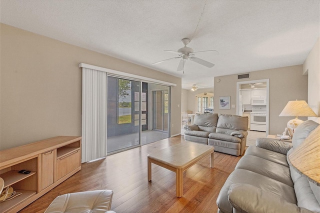 living room with ceiling fan, a textured ceiling, and light hardwood / wood-style flooring