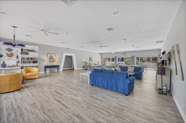 living room with ceiling fan, light wood-type flooring, and a textured ceiling