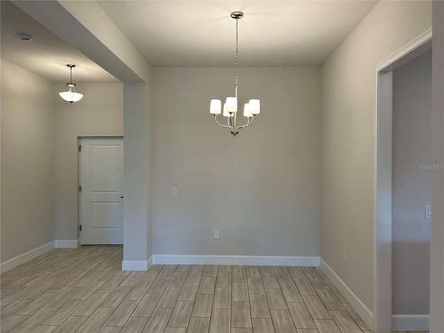 spare room featuring a chandelier, wood finish floors, and baseboards