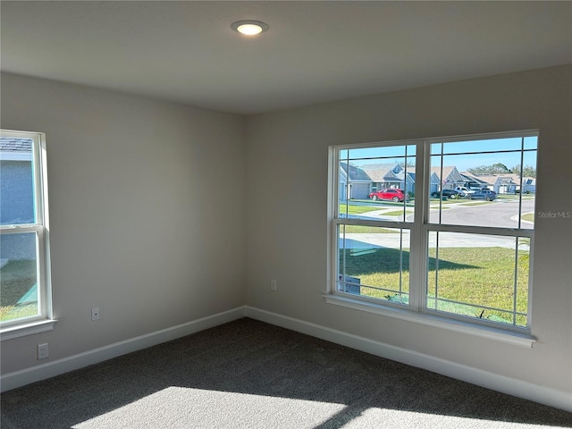 unfurnished room with dark colored carpet, a wealth of natural light, and baseboards