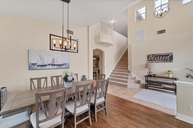 dining area featuring wood-type flooring, a towering ceiling, and an inviting chandelier