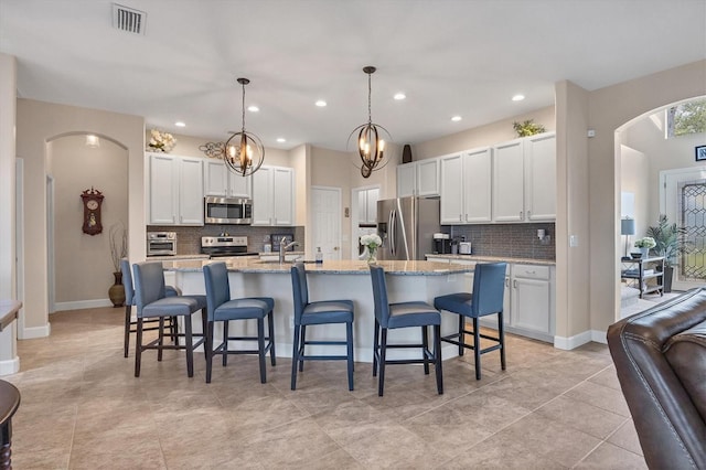 kitchen featuring appliances with stainless steel finishes, a breakfast bar, a kitchen island with sink, white cabinets, and hanging light fixtures