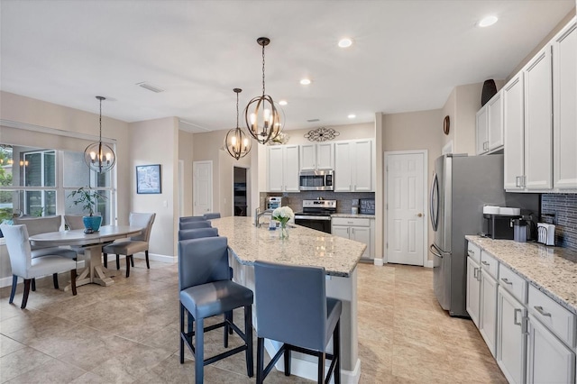 kitchen featuring decorative backsplash, stainless steel appliances, white cabinetry, and a breakfast bar area