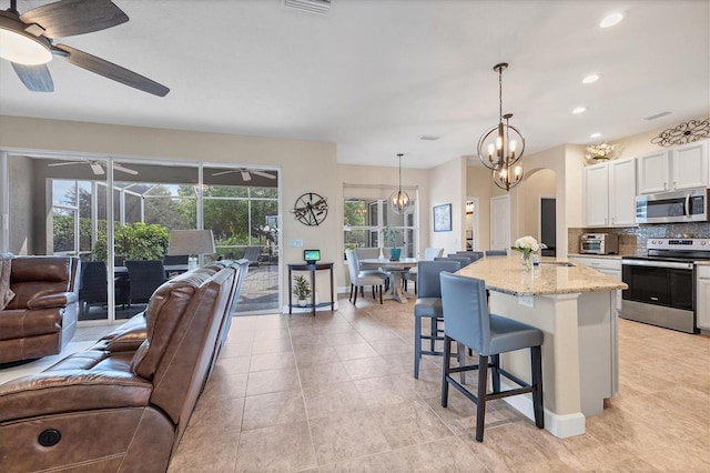 kitchen featuring white cabinetry, stainless steel appliances, an island with sink, decorative light fixtures, and a kitchen bar