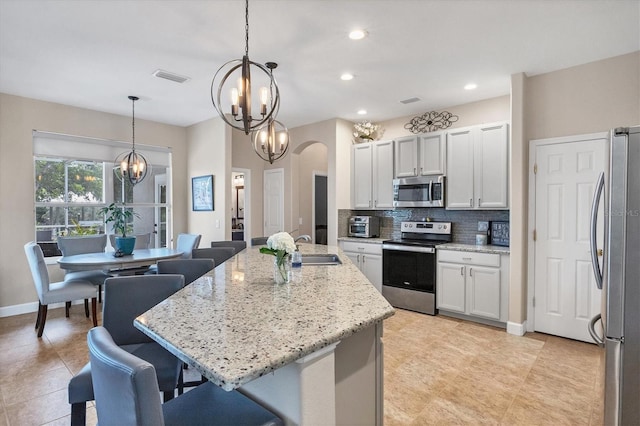 kitchen featuring pendant lighting, white cabinets, stainless steel appliances, and an island with sink