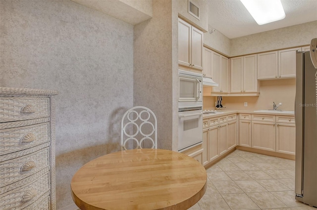 kitchen featuring white appliances, custom range hood, sink, light tile floors, and a textured ceiling