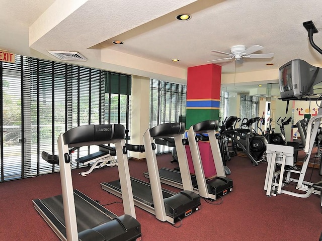 workout area featuring ceiling fan, dark carpet, a textured ceiling, and a tray ceiling