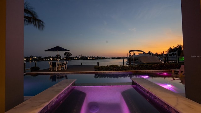 pool at dusk with an in ground hot tub and a water view