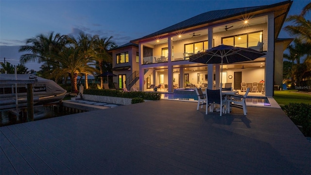 back house at dusk with ceiling fan, a swimming pool with hot tub, a balcony, and a patio