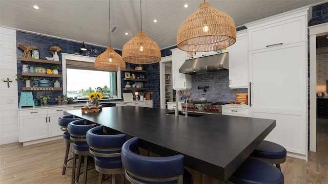 kitchen featuring a center island with sink, sink, hanging light fixtures, white cabinetry, and extractor fan