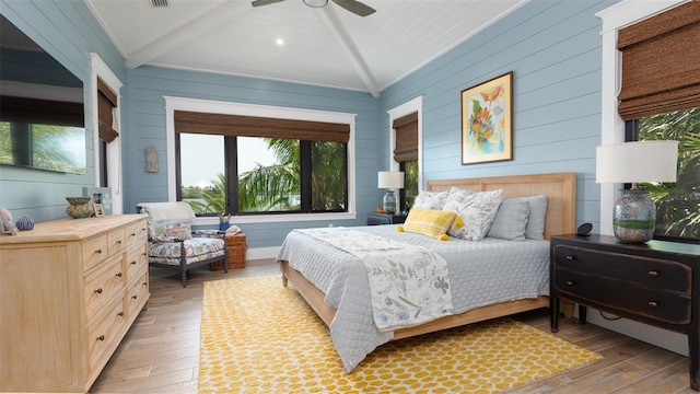 bedroom with hardwood / wood-style floors, wood walls, ceiling fan, vaulted ceiling with beams, and ornamental molding