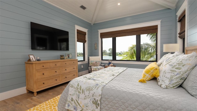 bedroom with beam ceiling, wood walls, and hardwood / wood-style flooring