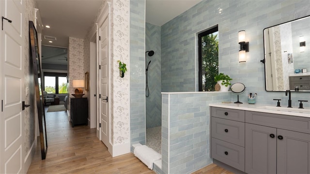 bathroom with tiled shower, wood-type flooring, vanity, and tile walls