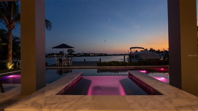 pool at dusk featuring an in ground hot tub and a water view