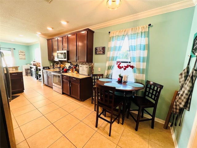 kitchen with dark brown cabinets, backsplash, stainless steel appliances, light tile floors, and ornamental molding