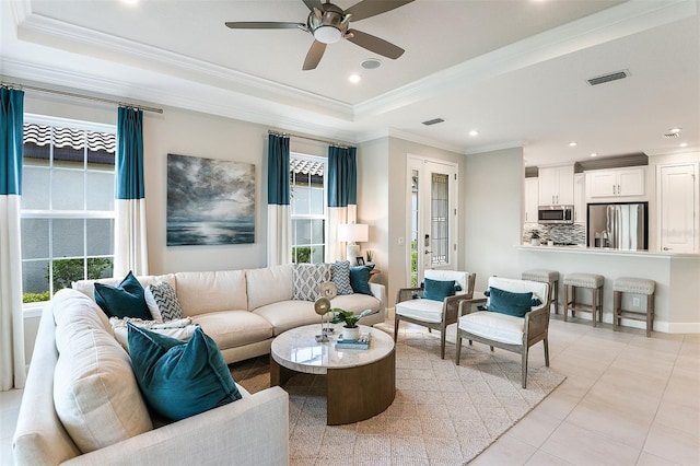 living room featuring ceiling fan, a raised ceiling, ornamental molding, and a wealth of natural light