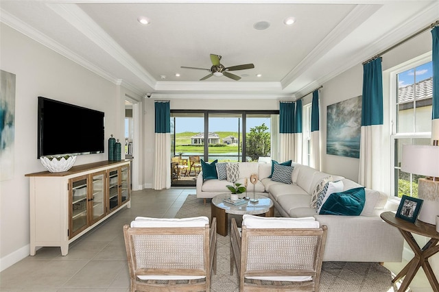 tiled living room with ceiling fan, ornamental molding, a wealth of natural light, and a tray ceiling