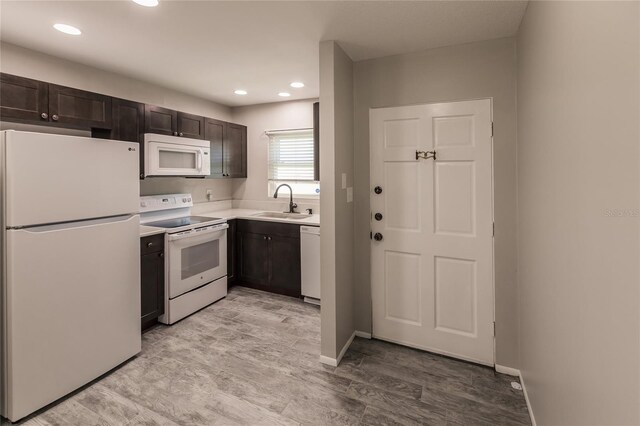 kitchen with sink, white appliances, dark brown cabinets, and light wood-type flooring