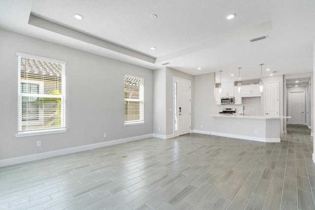 unfurnished living room featuring light wood-type flooring, a healthy amount of sunlight, and a raised ceiling