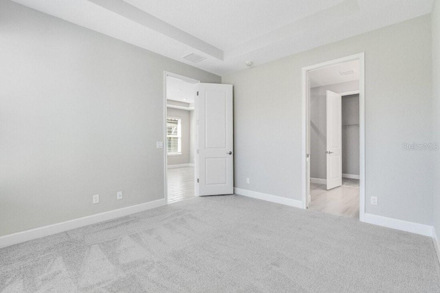 unfurnished bedroom with a walk in closet and light colored carpet