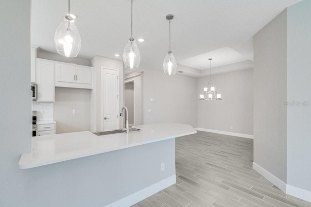 kitchen featuring white cabinetry, kitchen peninsula, decorative light fixtures, light hardwood / wood-style floors, and sink