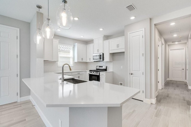 kitchen with appliances with stainless steel finishes, kitchen peninsula, hanging light fixtures, and white cabinets