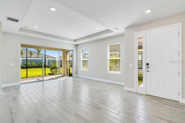 foyer with a raised ceiling, light hardwood / wood-style flooring, and a textured ceiling