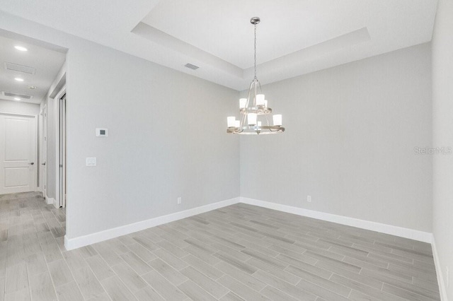 empty room featuring a tray ceiling and light hardwood / wood-style floors