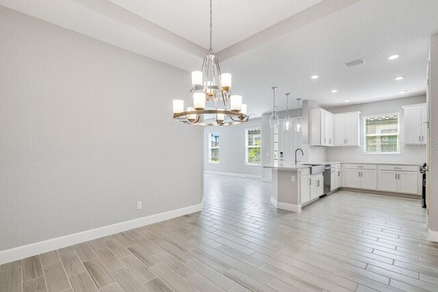 kitchen with stainless steel dishwasher, white cabinets, hanging light fixtures, and a healthy amount of sunlight