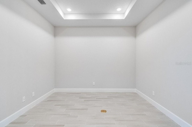 spare room with a tray ceiling and light hardwood / wood-style flooring