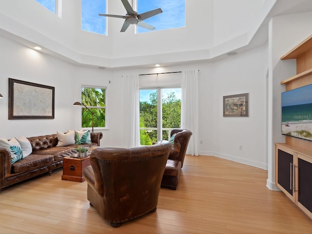 living room with a high ceiling, ceiling fan, and light hardwood / wood-style flooring