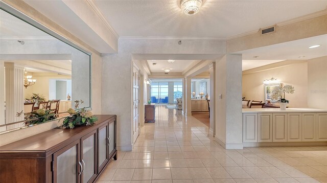 corridor with ornamental molding, ornate columns, light tile floors, and an inviting chandelier