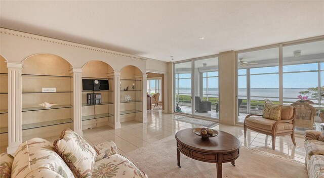 living room featuring built in features, a water view, decorative columns, a textured ceiling, and light tile floors