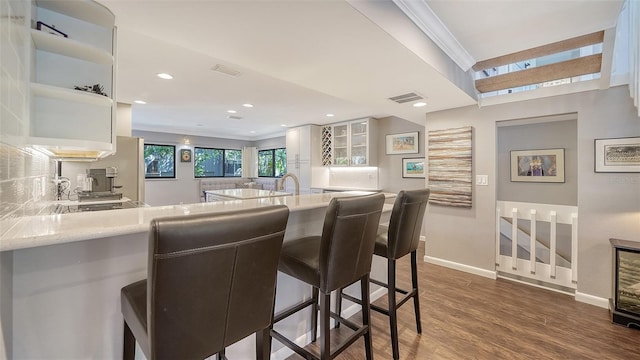 kitchen featuring kitchen peninsula, dark hardwood / wood-style floors, white cabinetry, a breakfast bar, and ornamental molding