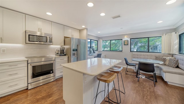 kitchen featuring stainless steel appliances, white cabinetry, a kitchen breakfast bar, dark hardwood / wood-style flooring, and a center island