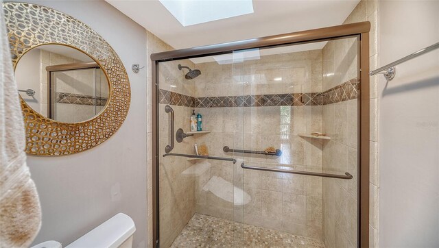 bathroom with a skylight, a shower with shower door, and toilet