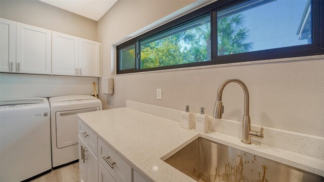 laundry area with sink, light hardwood / wood-style flooring, washer and dryer, and cabinets