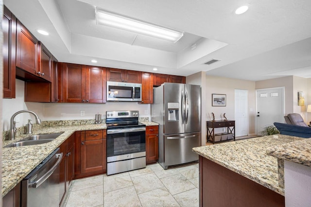 kitchen with light stone counters, appliances with stainless steel finishes, light tile floors, sink, and a tray ceiling