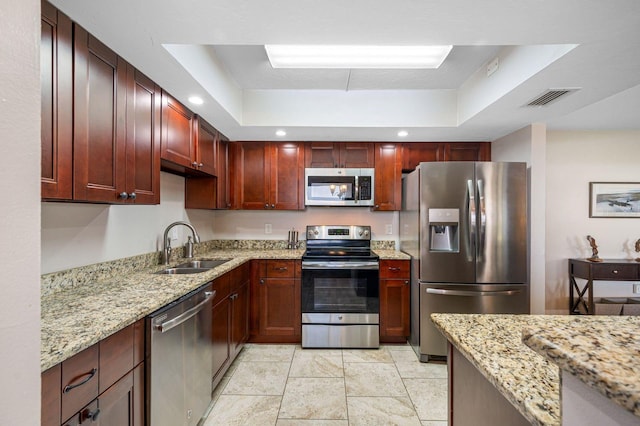 kitchen featuring a raised ceiling, stainless steel appliances, sink, and light stone counters