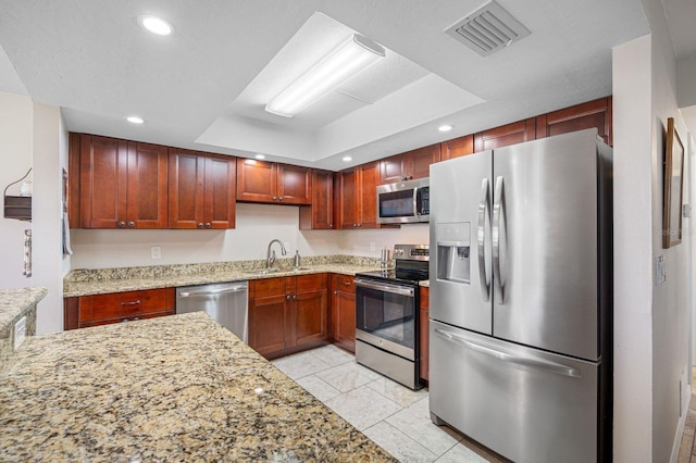 kitchen with light stone countertops, light tile flooring, appliances with stainless steel finishes, sink, and a raised ceiling