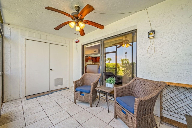 sitting room with ceiling fan, light tile flooring, and a textured ceiling