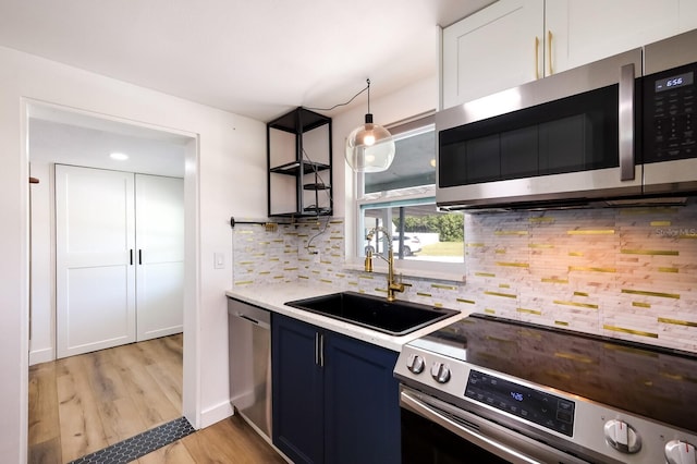 kitchen with blue cabinetry, appliances with stainless steel finishes, light hardwood / wood-style floors, tasteful backsplash, and sink