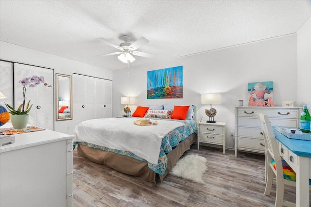 bedroom with hardwood / wood-style flooring, ceiling fan, a textured ceiling, and two closets