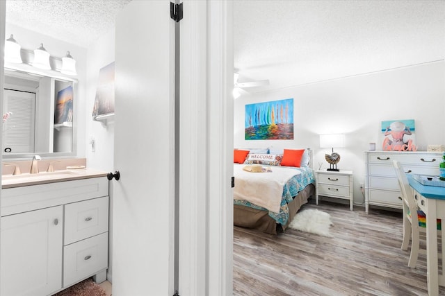 bedroom with a textured ceiling, ceiling fan, sink, and light wood-type flooring