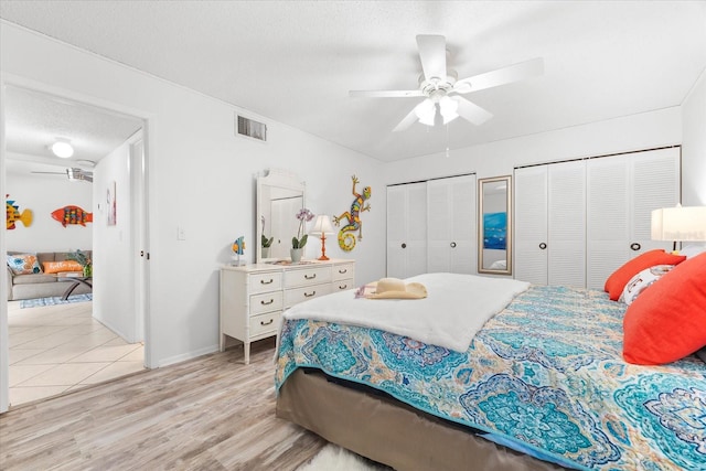 bedroom featuring light hardwood / wood-style floors, ceiling fan, and two closets