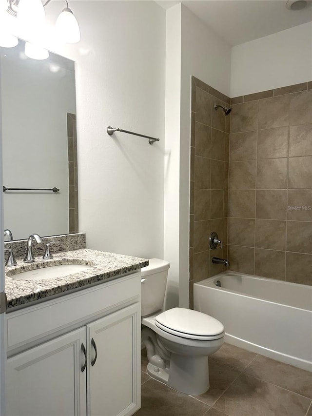 full bathroom with tiled shower / bath, toilet, tile floors, and vanity