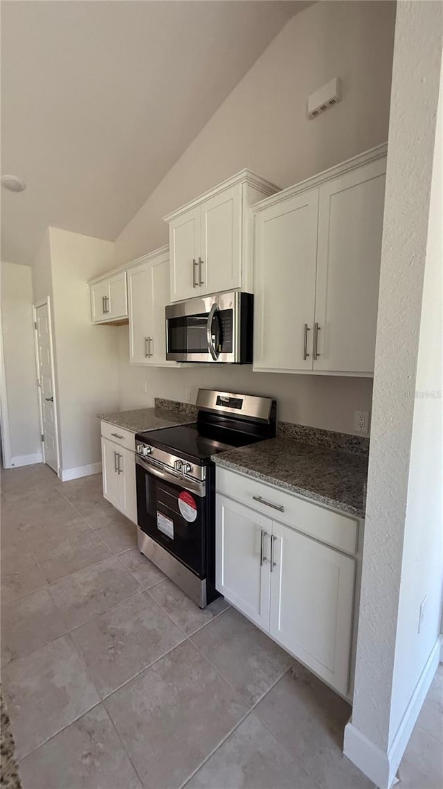 kitchen with appliances with stainless steel finishes, light tile patterned floors, white cabinetry, and lofted ceiling