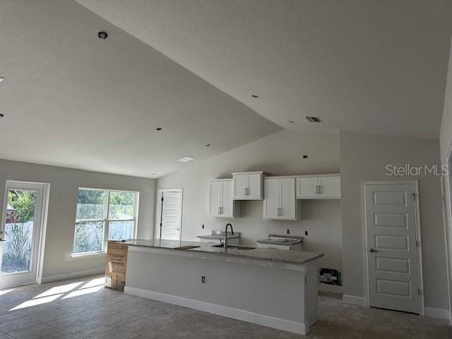 kitchen with vaulted ceiling, an island with sink, white cabinets, light stone countertops, and sink