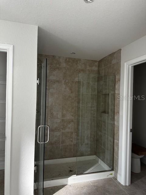 bathroom featuring a textured ceiling, a shower with door, tile patterned floors, and toilet